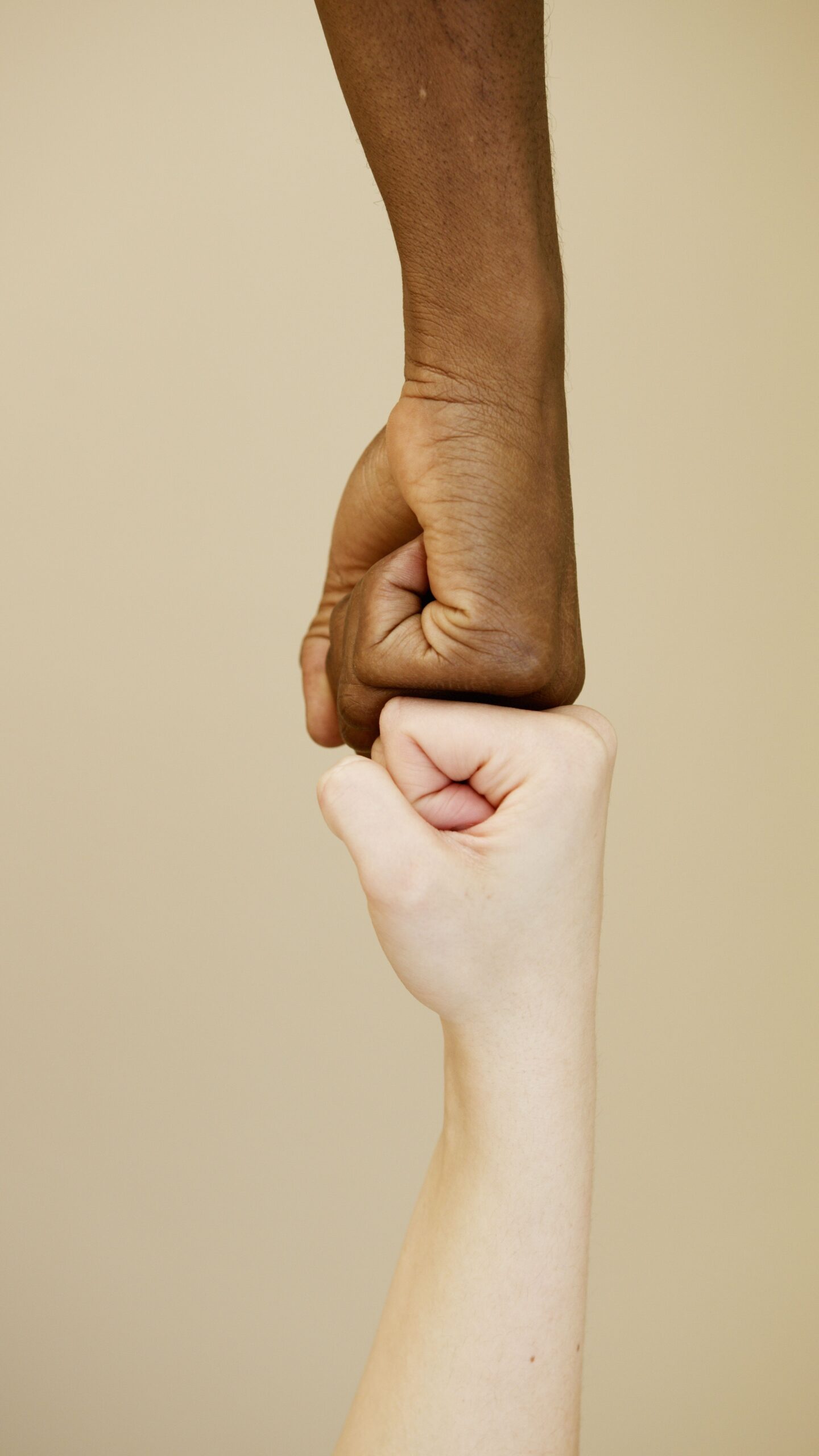 Close-up of two diverse hands in a fist bump on a beige background, symbolizing unity.