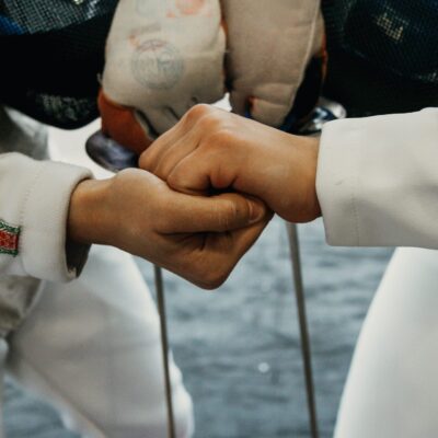 pexels-photo-5942132-5942132 Close-up of two fencers shaking hands in full gear before a fencing match indoors.