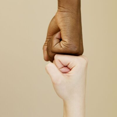 pexels-photo-8058539-8058539 Close-up of two diverse hands in a fist bump on a beige background, symbolizing unity.
